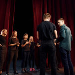 Group of actors in dark colored clothes on rehearsal in the theater.